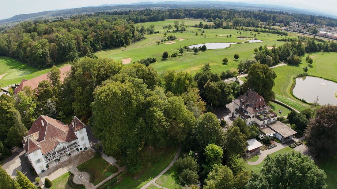 The estate from the air: the manor with its towers and baroque parterre at the left, the villa at the right, the adjoining golf course beyond